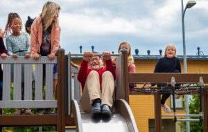 vanha mies laskemassa leikkipuiston liukumäestä lapset ympärillä